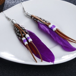 Detail of bohemian long feather earrings with purple beads and leather cords on white plate