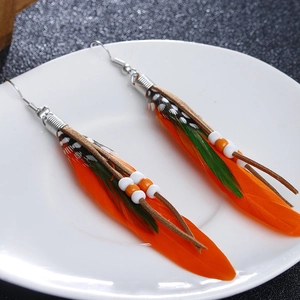 Detailed view of orange and green boho feather earrings with beads on a white plate