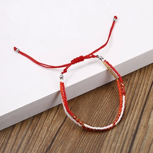 Détail du bracelet tressé rouge bohème avec perles colorées multicouches sur bois