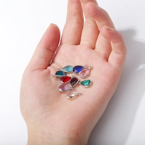 Close-up of colorful faceted teardrop birthstone charms with silver frames held in hand