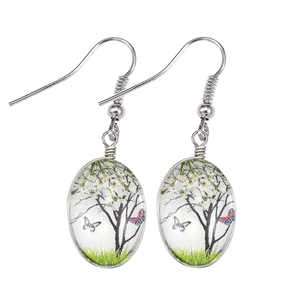 Detail of oval glass earrings featuring tiny white flowers and butterflies in a silver frame