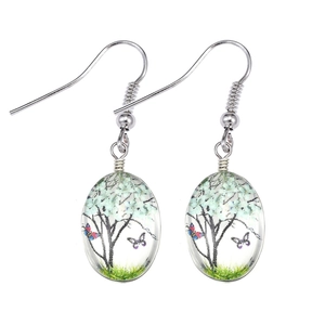 Macro shot of glass earrings featuring white tree and butterfly miniature landscape
