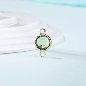 Detail of a gold-plated round link charm with a faceted green crystal and double hoops