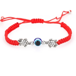 Detalle de pulsera de cuerda roja tejida con ojo de la suerte y amuletos de tortuga plata