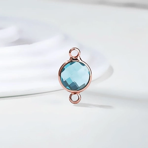 Macro detail of a rose gold birthstone charm with light blue faceted crystal and dual loops