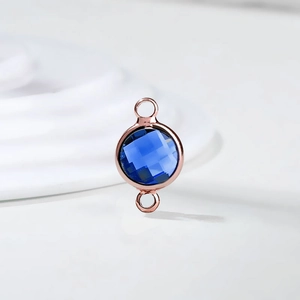 Detail of rose gold double-loop connector with faceted blue birthstone crystal for DIY jewelry