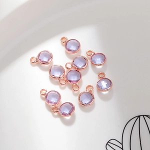 Macro view of 10 purple 6mm faceted crystal pendants with rose gold frames in a ceramic dish