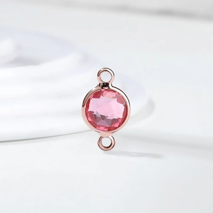 Macro view of a faceted pink crystal birthstone charm in a rose gold dual-loop setting