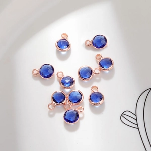 Macro shot of 6mm deep blue faceted crystal charms in rose gold plated frames for DIY jewelry