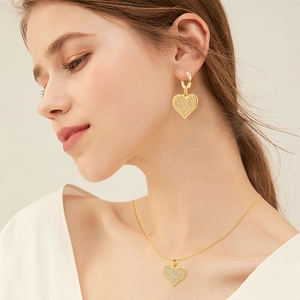Close-up of heart-shaped gold pendant earrings and necklace with pave-set crystals