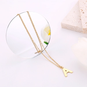 Dettaglio macro della collana dorata con pendente iniziale A su tulipano bianco e specchio