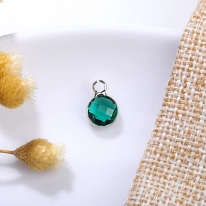 Macro shot of 6mm green birthstone crystal pendant with silver setting on ceramic background