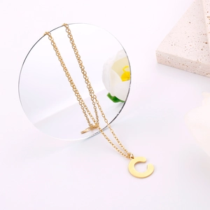 Dettaglio macro della collana con ciondolo lettera C dorata su specchio e pietra