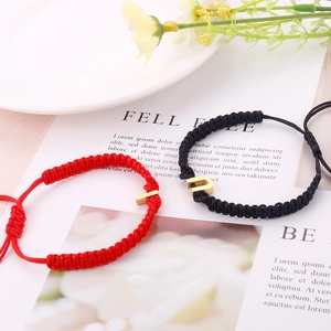 Detail of red and black braided bracelets with gold bar and U-shape metal accents
