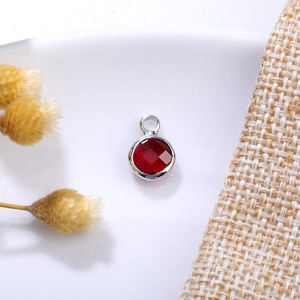 Macro detail of 6mm red birthstone charm with silver-plated copper edge and hanging loop