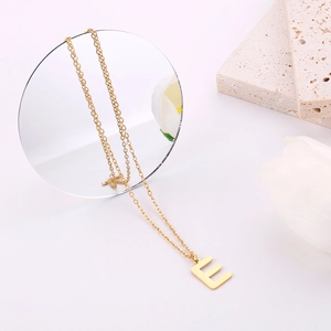 Dettaglio del ciondolo minimalista con lettera E in oro e finitura spazzolata