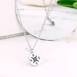Detailed close-up of a stainless steel compass pendant necklace on a white marble surface