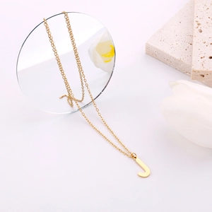 Dettaglio di una collana minimalista con ciondolo a lettera J dorata e catena a O