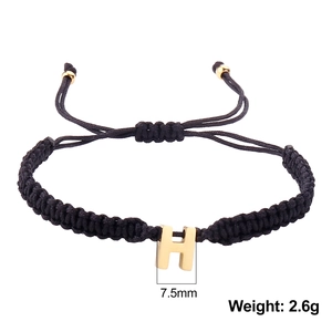 Detail of adjustable black woven rope bracelet with gold letter H pendant charm