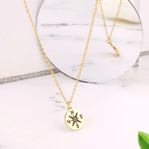 Detailed shot of golden compass pendant necklace on marble surface with mirror reflection