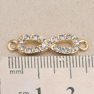 Nahaufnahme eines goldenen Unendlichkeit-Anhängers mit Strass und Maßtabelle