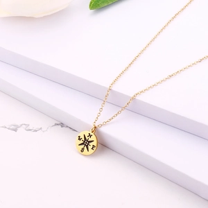 Close-up of golden compass pendant necklace with N, E, S, W directional engravings