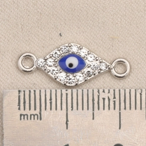 Makroaufnahme von Evil Eye Verbinder mit blauen Steinen und Kristallen neben einem Lineal