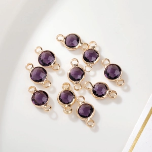 Close-up van tien paarse geboortesteen bedeltjes met gouden lussen voor DIY-sieraden