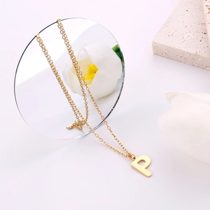 Dettaglio di un ciondolo a lettera P in oro lucido su una catena fine dallo stile minimal