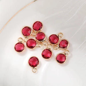 Macro shot of 10 red faceted 6mm birthstone charms with gold plating in a white ceramic dish