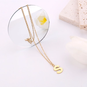 Dettaglio della collana con ciondolo a lettera S dorata tra fiori e elementi in pietra