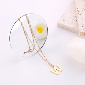 Dettaglio di una collana dorata con ciondolo lettera W e decorazione elegante
