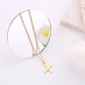 Dettaglio della collana dorata con ciondolo a lettera X minimalista su sfondo bianco chic