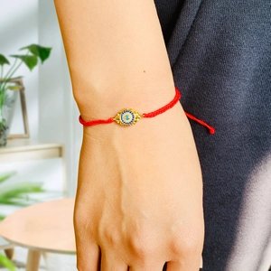 Close-up of red braided rope bracelet with a gold evil eye charm and inlaid crystals