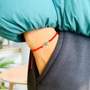Close-up of red braided rope bracelet with gold-plated Evil Eye charm worn on the wrist