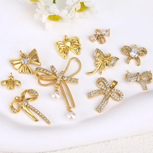 Détails de pendentifs dorés en forme de nœud et d'abeille avec strass et perles sur plateau