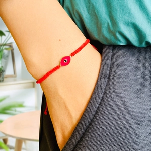Detail of red braided Evil Eye bracelet with enamel palm charm worn on a wrist