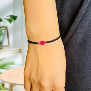 Detail of hand-woven black cord bracelet with pink evil eye charm on a female wrist