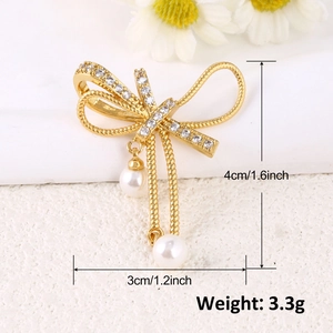 Détail d'une broche nœud doré avec strass et perles blanches, dimensions de 4x3cm