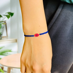 Close-up of woven blue bracelet with red evil eye charm on wrist for detailed view