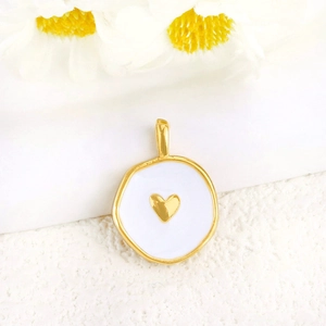Detail of white enamel round pendant with gold heart pattern and metal loop