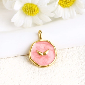 Macro shot of gold plated pendant with pink enamel heart and tiny wings detail