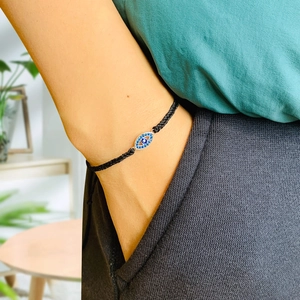Detail of hand-woven bracelet with sparkling blue evil eye charm on model's wrist
