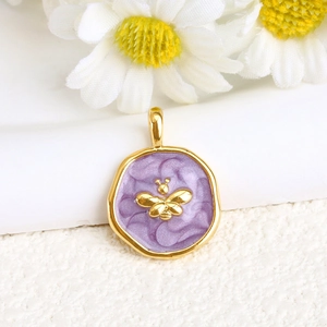 Detailed close-up of golden bee pendant with purple enamel on white daisies background