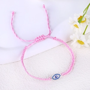 Macro view of adjustable pink braided rope bracelet with pavé evil eye charm details