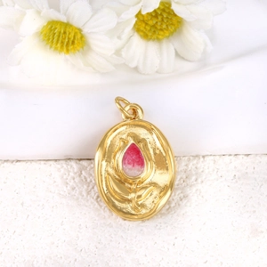 Macro shot of oval gold-plated tulip pendant with embossed floral detail and pink resin