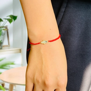 Detail of red braided cord bracelet with gold Hamsa Hand and blue evil eye stone