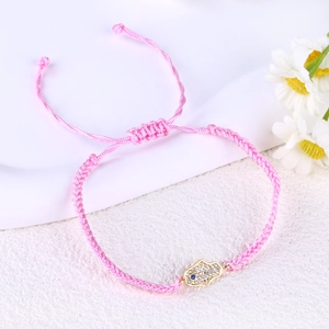 Detail of pink woven bracelet with gold Hamsa Hand charm and blue evil eye accent