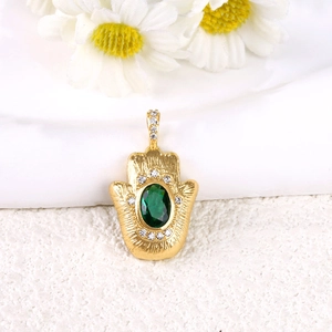 Dettaglio macro di un ciondolo mano di fatima placcato oro con pietra verde smeraldo