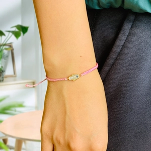 Close-up of pink braided bracelet with a gold Hamsa Hand and Evil Eye charm on a wrist